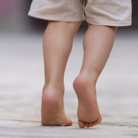 A child walks with their right foot lifted and leaned forward